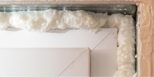 A close-up of a door frame with spray foam insulation filling the gaps between the frame and wall.